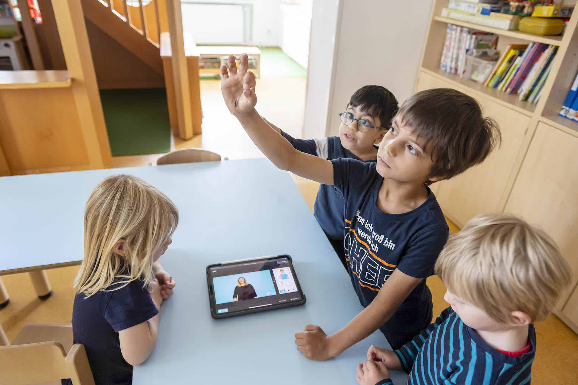 Kinder gebärden „gut” in der Kita während das SIGNdigital Gebärdenvideo auf eine Tablet abgespielt wird.
